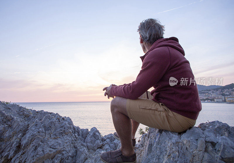 日出时，一个成熟的男人坐在海上的岩石脊上