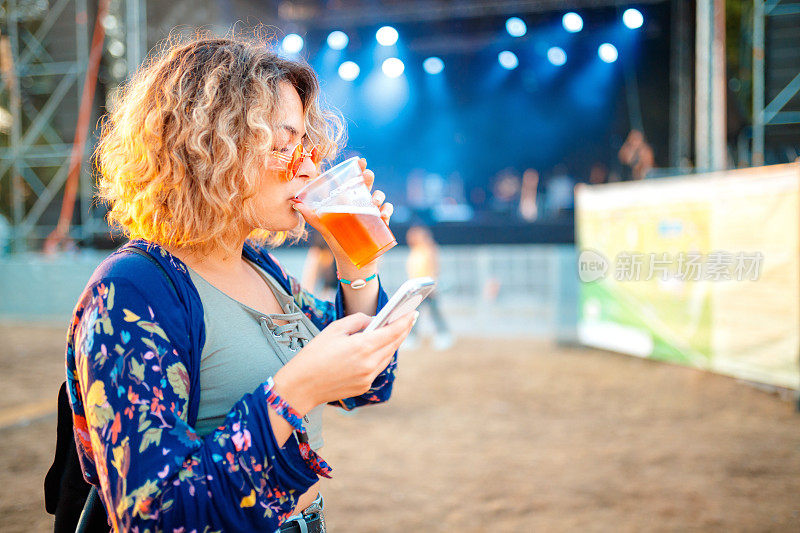 年轻女子在露天音乐节上喝啤酒发短信