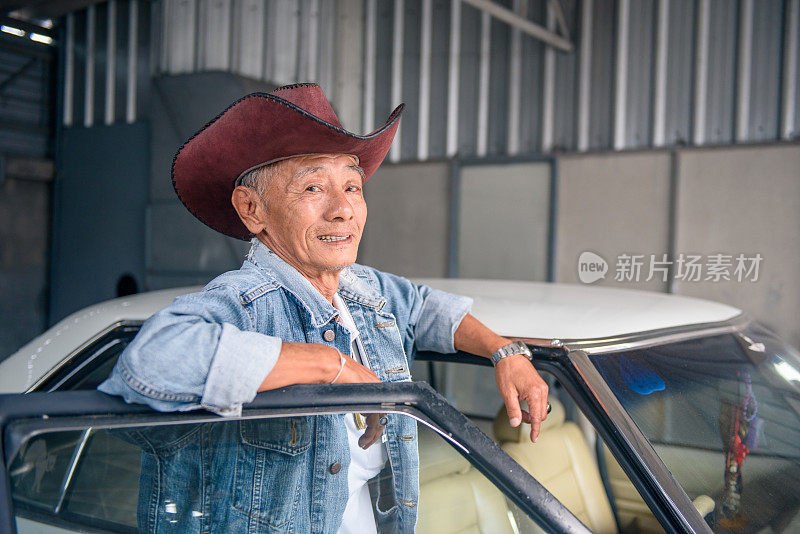 年长的亚洲男人在复古牛仔夹克摆姿势与古董车