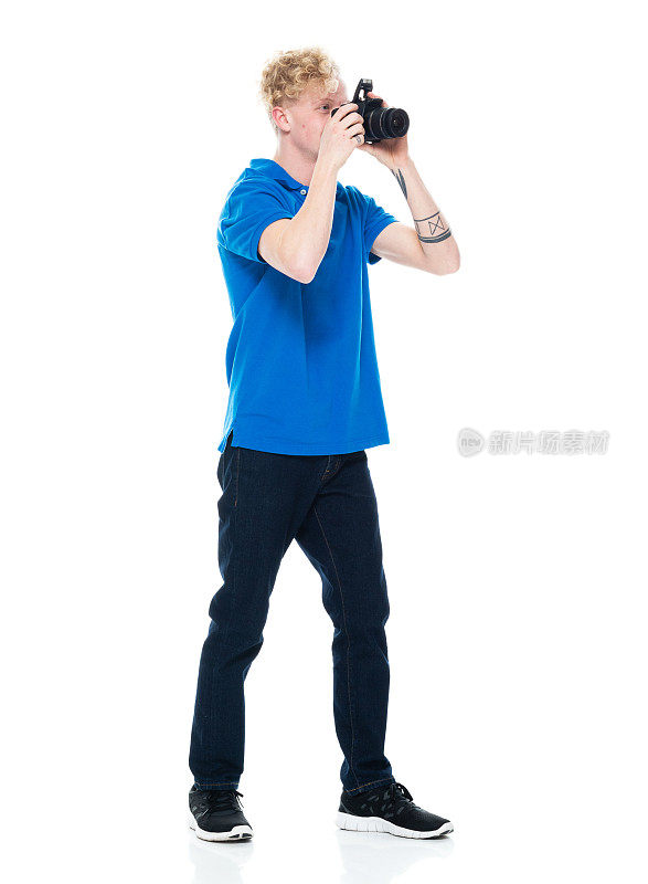 白人年轻男性摄影师穿着牛仔裤，手持相机站在白色背景前
