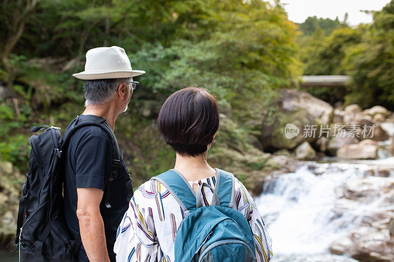 一对老年夫妇徒步旅行，欣赏瀑布