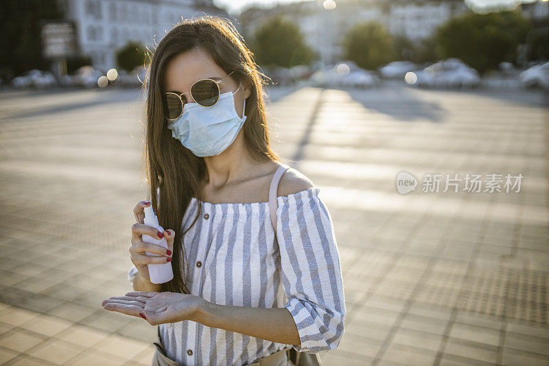 一名年轻女子戴着外科口罩，手上涂着洗手液，在封锁期间站在空荡荡的城镇广场上