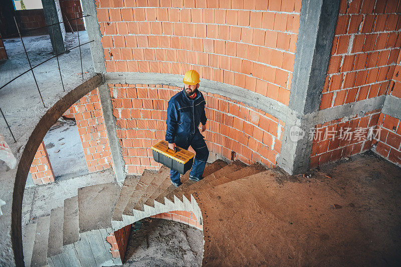 年轻男性建筑工人在建筑工地搬运工具箱