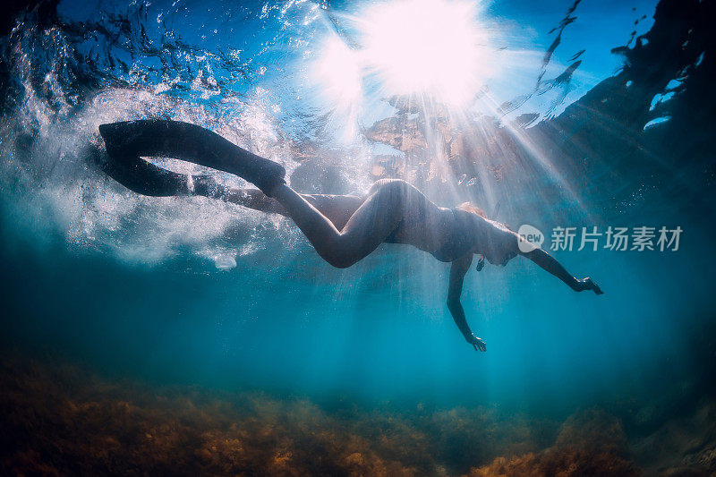 带着脚蹼和面具的年轻女子在阳光照耀下的蓝色海洋中游泳。在夏天的海面下浮潜
