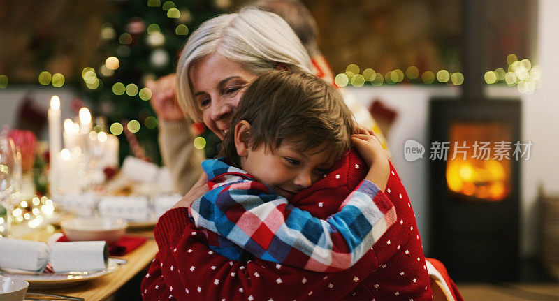 在家里的圣诞晚宴上，一位深情的老年妇女拥抱着她的孙子