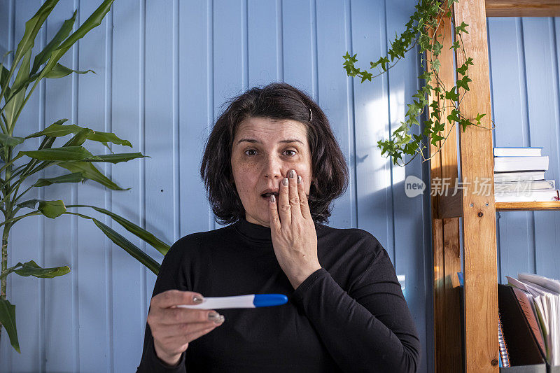 中年妇女看着怀孕测试享受惊喜的结果显示积极的母亲兴奋。受精或试管受精的概念