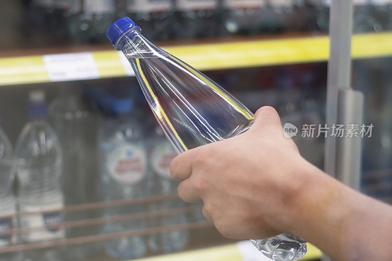 在一个商店橱窗的背景上，一个男人手里拿着一个装着纯矿泉水的塑料瓶。