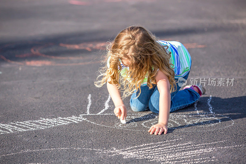 小女孩在柏油路上用粉笔画画