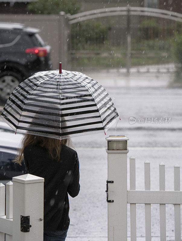 少女撑着伞在雨中走在街上。纽约皇后区