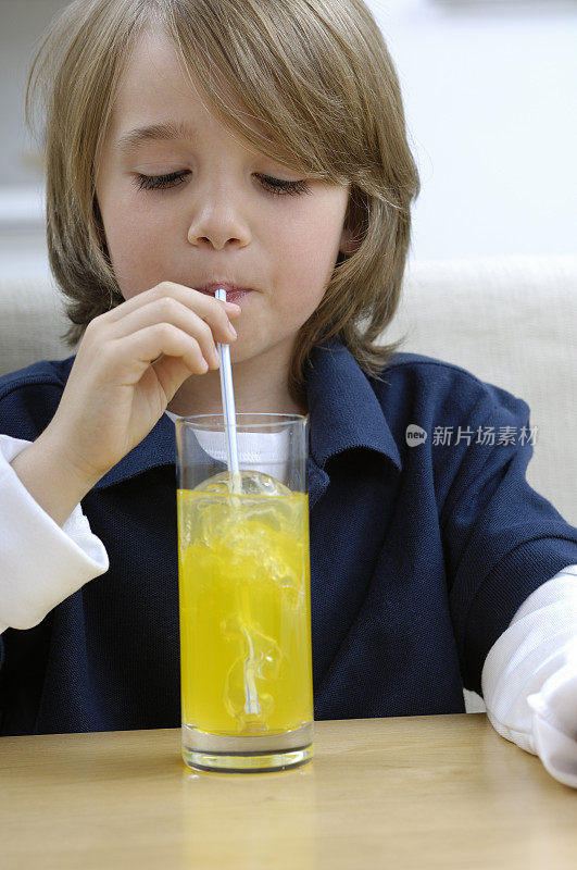 小男孩用吸管喝着一杯橙汁