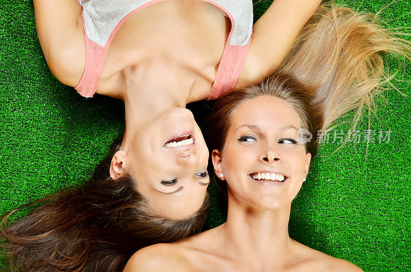 两个快乐的女性朋友躺在草地上微笑着
