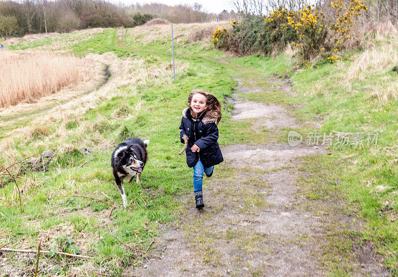 一个六岁的小女孩和狗在乡间小路上奔跑