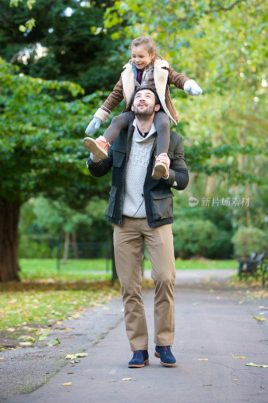 小女孩背着她爸爸的肩膀在公园里散步