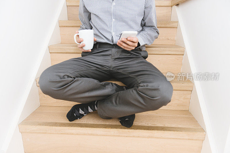 男子盘腿坐在木台阶上用手机发短信。