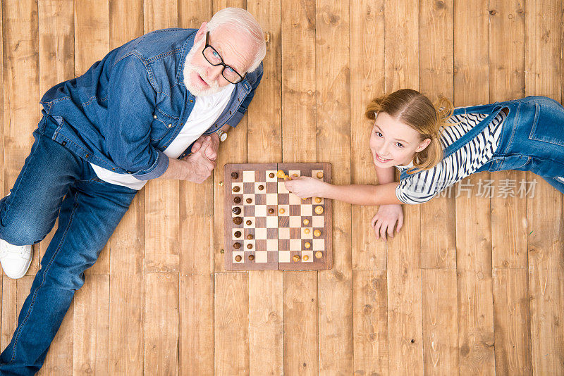 高角度的微笑女孩与高级男子下棋在木地板上