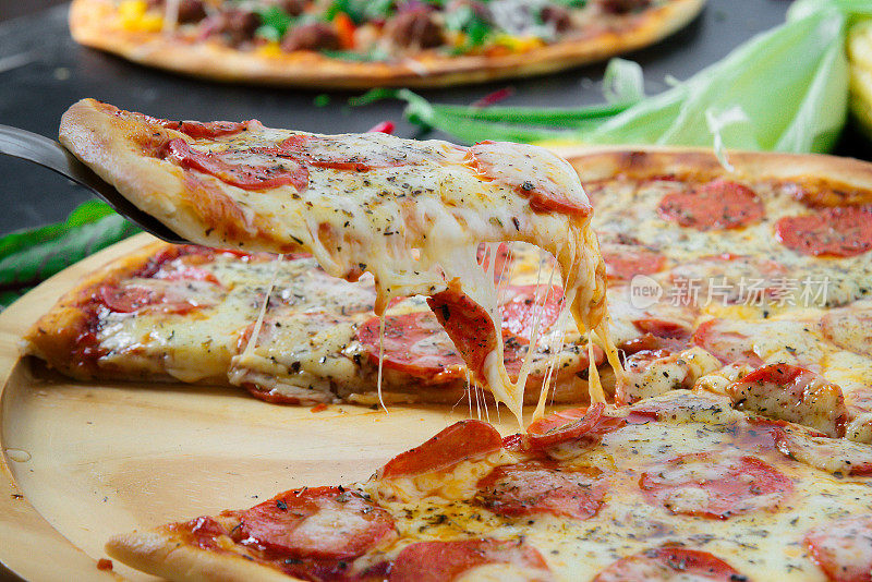 在一张质朴的深色木桌上，放着热披萨和融化的奶酪。