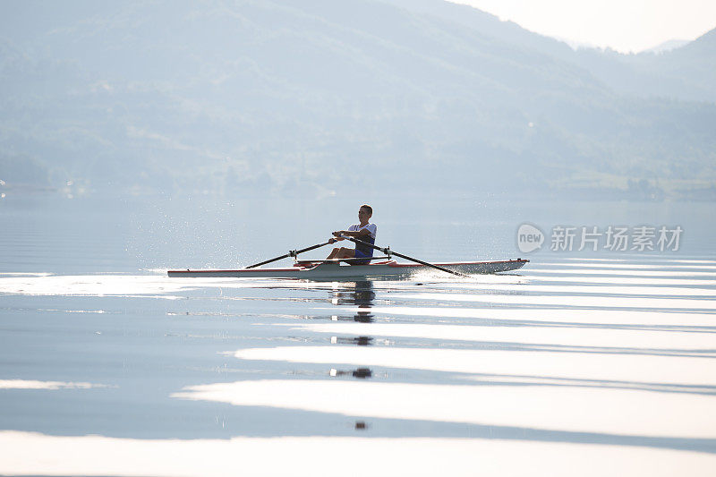 一位年轻的单人赛艇选手在宁静的湖面上划桨