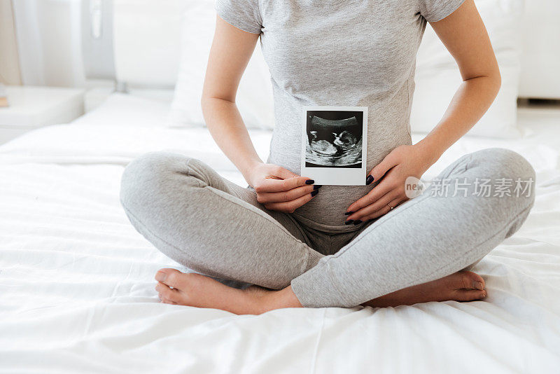 怀孕年轻妇女坐和显示超声波照片的特写