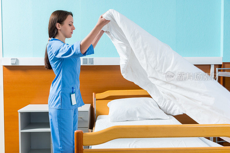 身穿蓝色制服的年轻护士在病床上换床单
