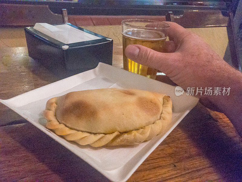 拿着一杯啤酒的男人。肉馅卷饼和餐巾架。