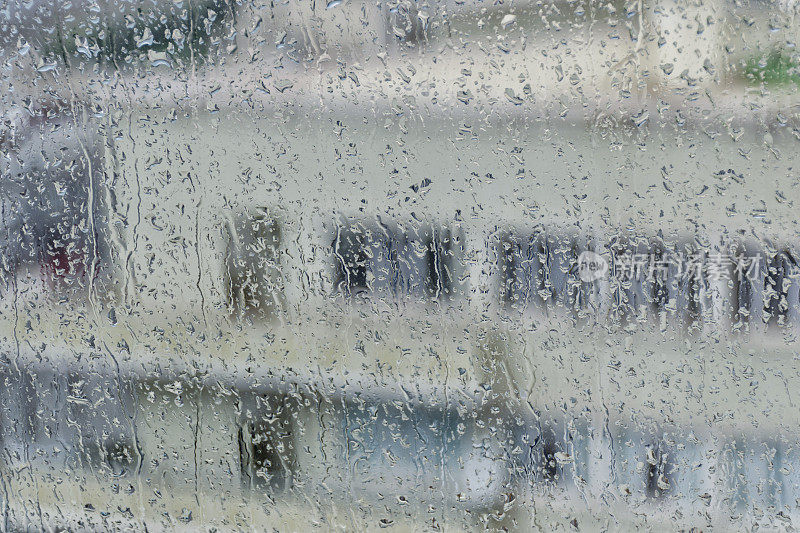 一个多层建筑的剪影与白色的墙壁和窗户的背景与雨条纹湿玻璃。