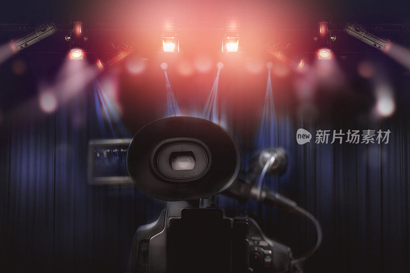 专业摄像机的后部，在电视演播室背景悬挂一套灯光。
