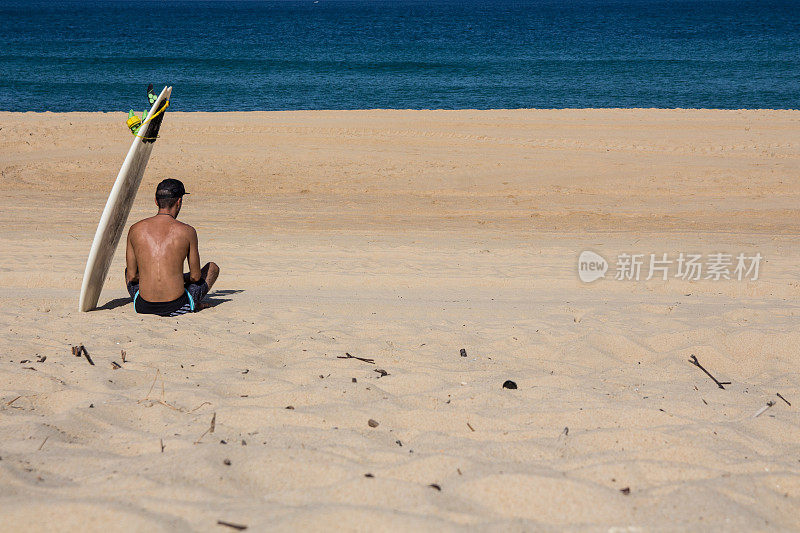 一个冲浪者坐在空荡荡的海滩上