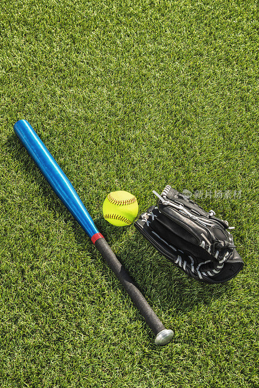 低头看着草地上一个崭新的黄色垒球，黑色手套和铝制球棒
