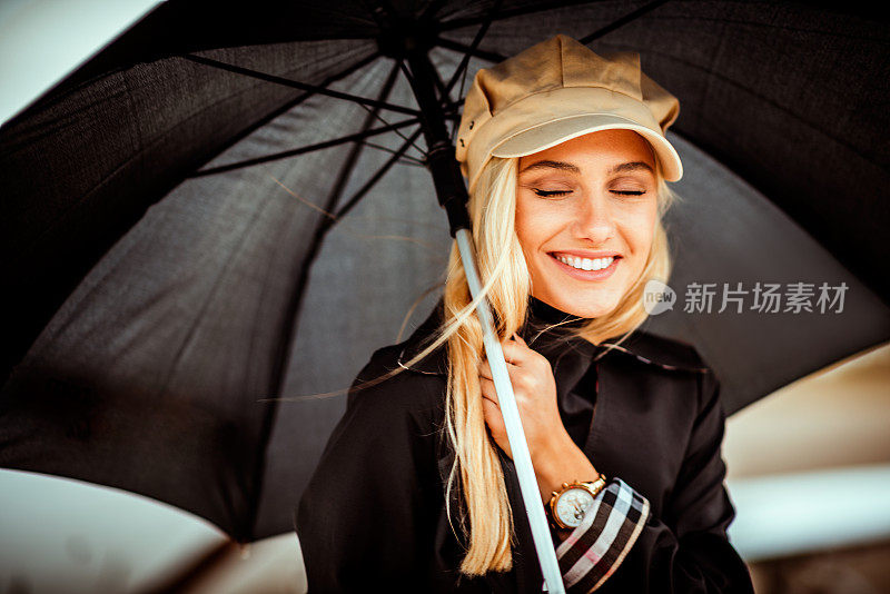 一个年轻漂亮的金发女人撑着一把黑伞站在机场跑道上