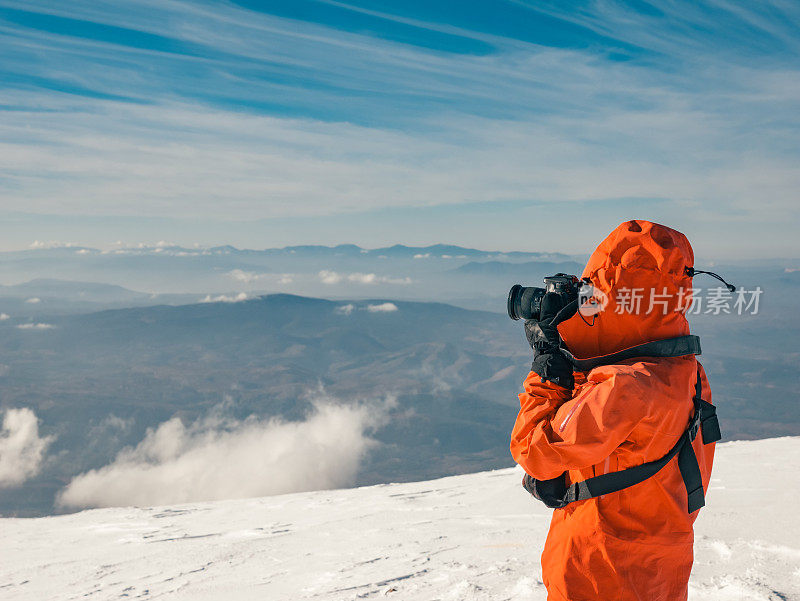 冬季日出时，女性高山攀登者在高海拔的山峰上拍照