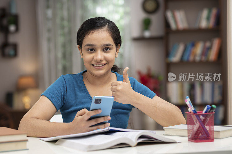 一个十几岁的女学生在家里用手机学习:-库存照片