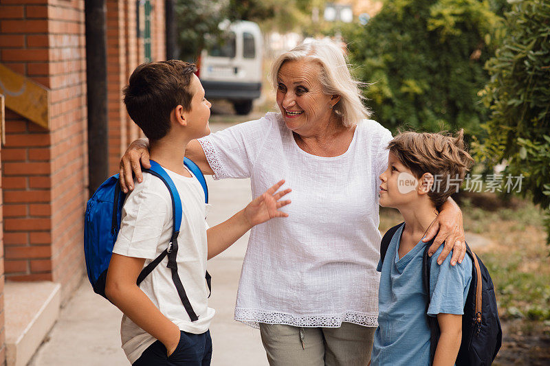 一位金发的老妇人在学校门口和她的孙子孙女们说话。