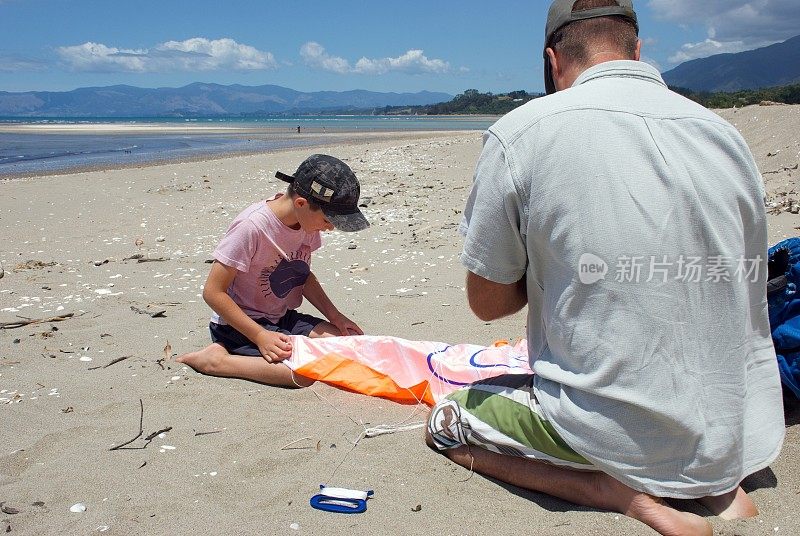 夏天的海滩上，父亲帮儿子解开风筝的包裹