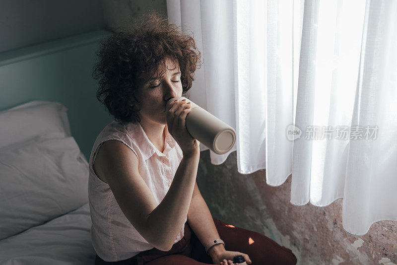 一个白种女人从床上的水瓶里喝水