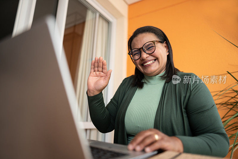 快乐的成熟女人在家里做视频通话的时候挥舞着笔记本电脑