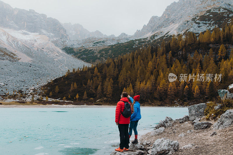 女游客和男游客呆在岩石上，欣赏阿尔卑斯山上冰封的高山湖泊的风景
