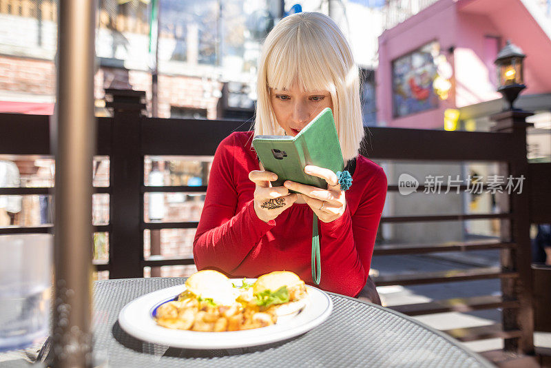 戴着铂金假发、穿着红色衬衫的年轻女子在户外咖啡馆拍摄食物