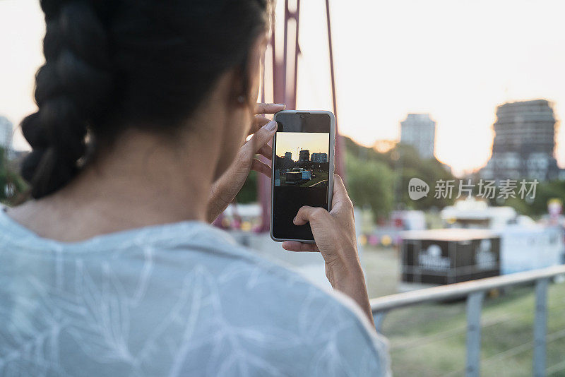 在户外用智能手机拍照的女人的后视图