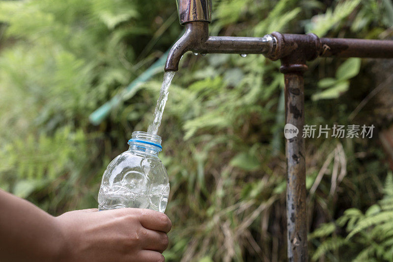 年轻的手用塑料瓶从一个老的缓慢流动的水龙头里吸水，充满耐心——缺水——节约用水的概念。