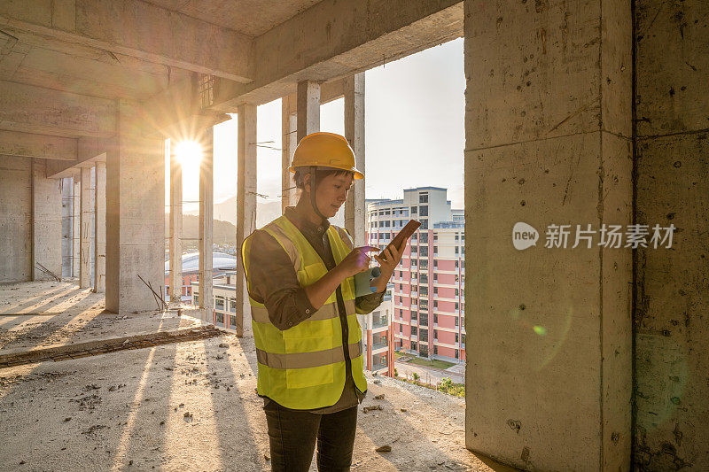 一位亚洲女建筑工人正在工地上使用手机