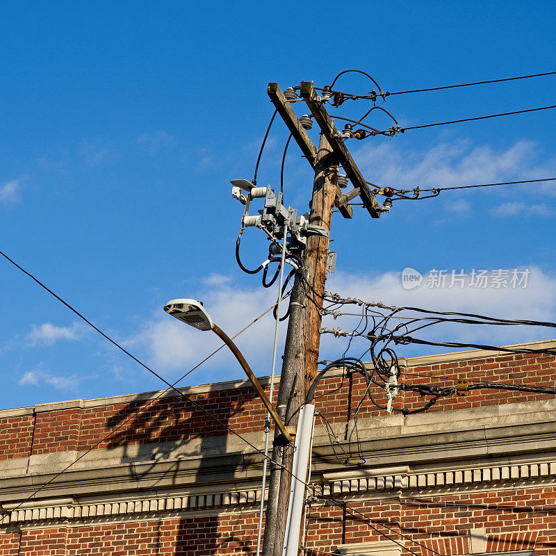 老旧杂乱的电线和电话线挂在一根老式的杆子上，砖砌的屋顶线和蓝色的天空