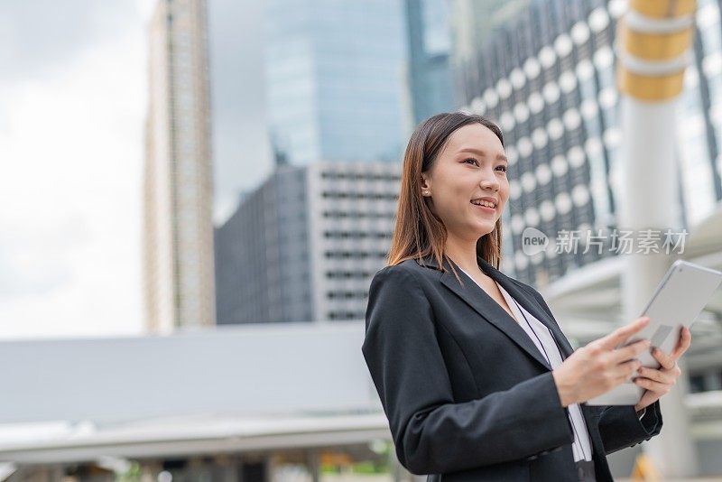 在曼谷市中心的一个商务区，年轻迷人的亚洲职业女商人女士带着美好的微笑在她的平板电脑上阅读了最新的市场和销售报告后仰望天空