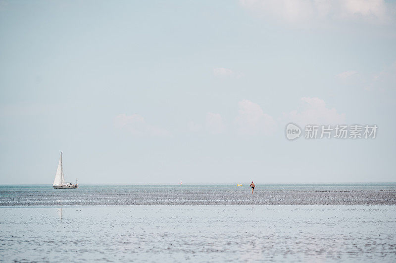 远处有一个人正在退潮时走过瓦登海。一艘帆船在地平线上缓缓航行