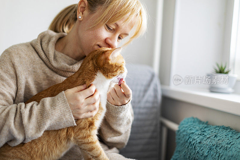 年轻的成年妇女和姜黄色的猫在家里