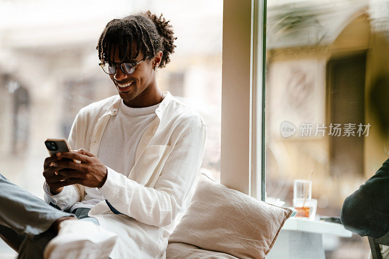 年轻的非洲裔美国人在咖啡馆里微笑着用手机