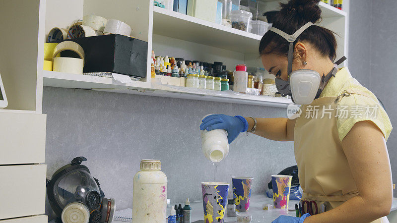 在创意工坊里，一个女人正在把容器里的材料倒进一个一次性杯子里，准备工作