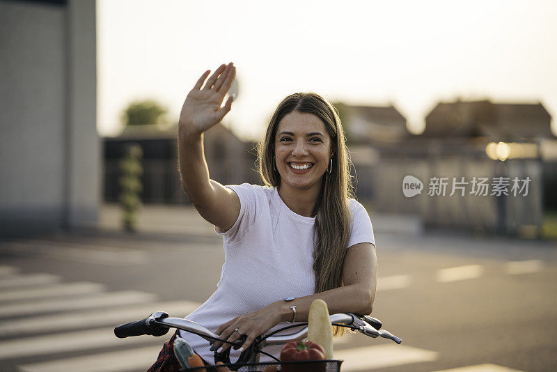 漂亮的年轻女子坐在自行车上向人挥手。