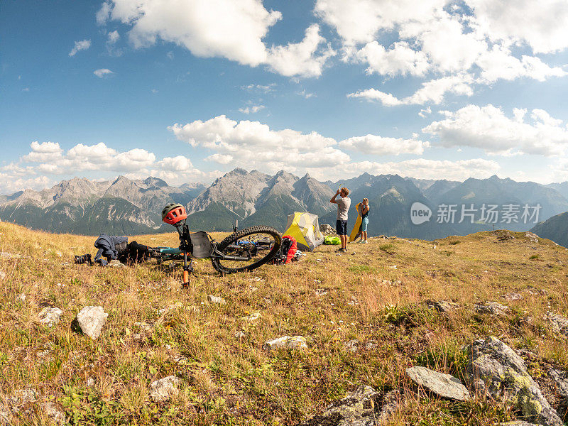 一对夫妇在瑞士阿尔卑斯山骑自行车，日落时分在山顶搭起帐篷