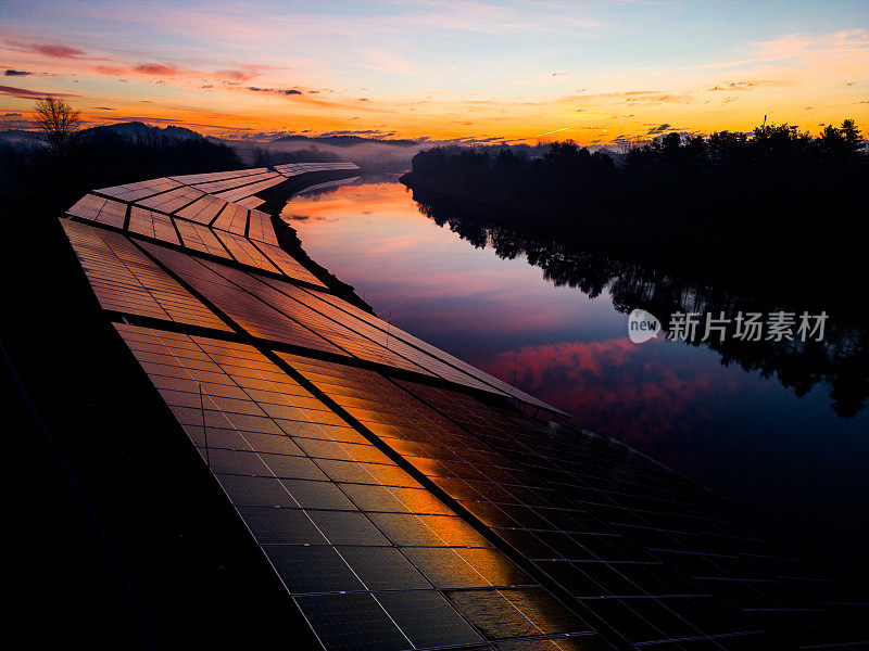 日落时河边的太阳能发电站。日落时太阳能电池板和河流的剪影。替代电源