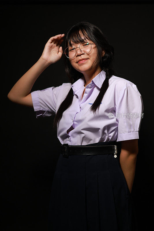 微笑的脸。年轻的亚洲女学生穿着校服，戴着黑色背景的眼镜。女学生肖像，工作室横幅标题。学校孩子的脸，拷贝空间。